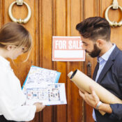 Real estate agent showing house floor plan to client outside property with for sale sign