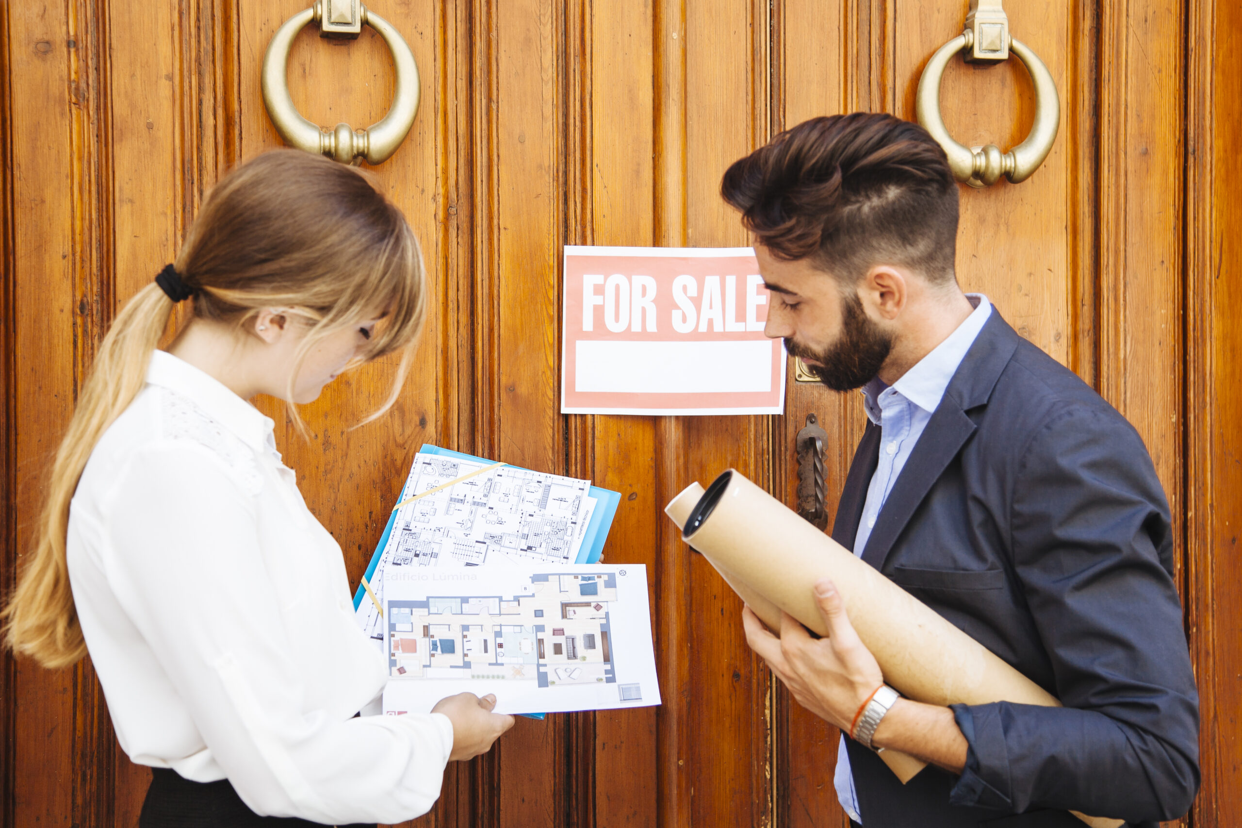 Real estate agent showing house floor plan to client outside property with for sale sign