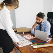 Real estate agent discussing property plans with client, for sale sign on desk