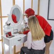 Professional makeup artist drawing face chart for client at elegant white vanity table with cosmetics