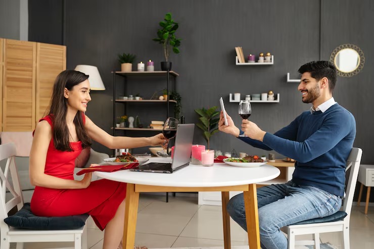 Happy couple enjoying romantic virtual dinner date with wine and laptop in modern home setting