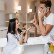 Frustrated woman gesturing towards a man who is ignoring her while talking on a smartphone in a modern kitchen setting.